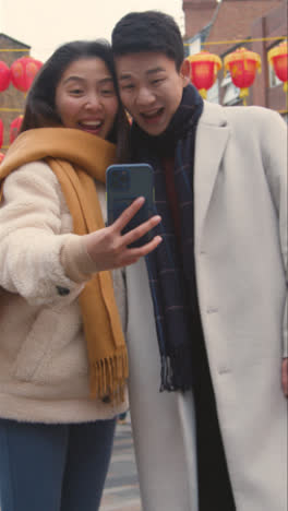 Video-Vertical-De-Una-Joven-Pareja-Asiática-De-Vacaciones-Posando-Para-Un-Selfie-En-Un-Teléfono-Móvil-En-Chinatown,-Londres,-Reino-Unido